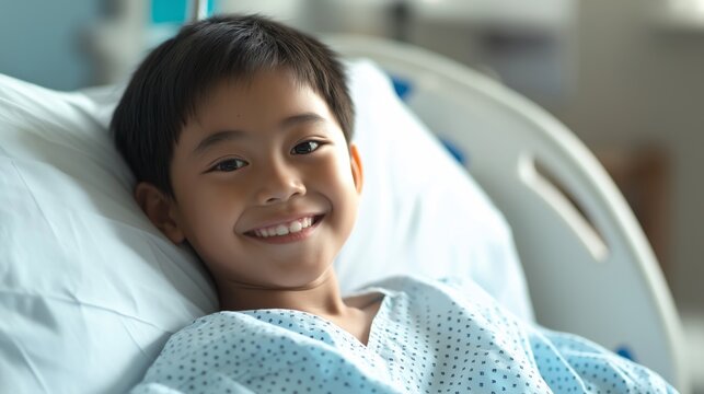 Central Asian Boy Smiling While Lying in Hospital Bed Wearing Patient Gown, Healthcare and Recovery Scene