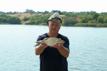 Fisherman holding caught fish near lake outdoors
