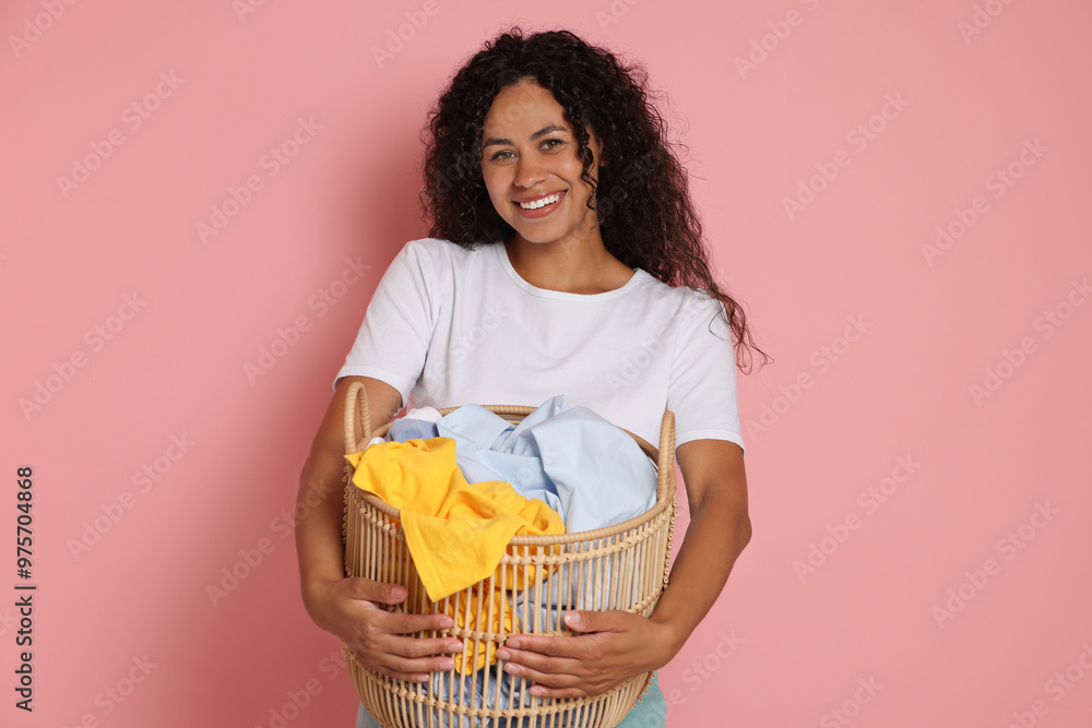 Wall mural Happy woman with basket full of laundry on pink background