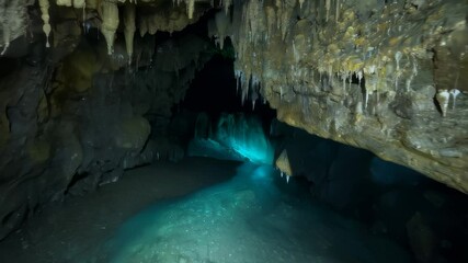 Natural subterranean cave with stalactites and stalagmites zooms in with blue glowing liquid and elements on floor - Powered by Adobe