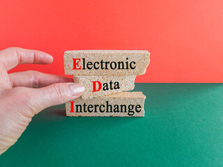 Concept words EDI electronic data interchange on brick blocks. Beautiful green table, red background. Businessman hand. Business and EDI electronic data interchange concept.