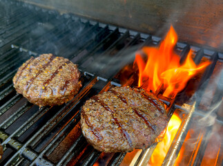 Wagyu beef hamburgers patties sizzling on a flaming gas grill barbecue. 