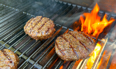 Wagyu beef hamburgers patties sizzling on a flaming gas grill barbecue. 