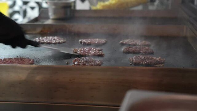 The chef is flipping the cooking burger patties. Vertical size