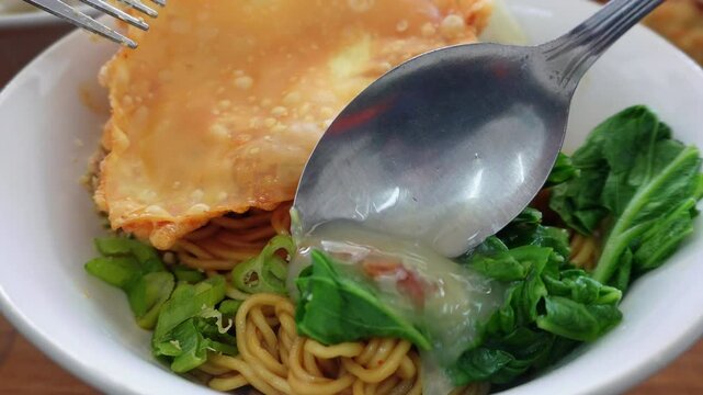 A bowl of noodles with pakcoy vegetables and fried wonton crackers