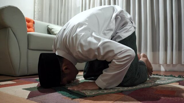 Young asian man with Muslim cap performing namaz or salat prayer sitting on knees at home