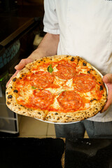 Chef holding italian salami pizza with cheese