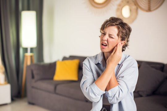 Sick woman having ear pain at home, upset female rubbing sore auricle with hand and frowning, suffering from otitis and acute ache, closeup shot