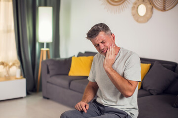 A man holding his face in pain due to a toothache. His expression reveals his suffering as he tries...