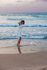 Fototapeta premium Happy traveler girl in a white summer dress enjoying a tropical paradise beach with turquoise sea.
