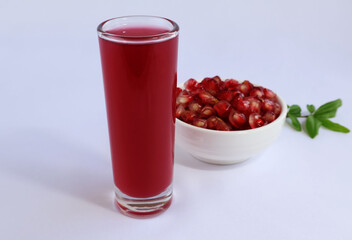 dark red juice in a glass Next was a bowl of red pomegranate seeds, with branches and leaves placed on a white background.

