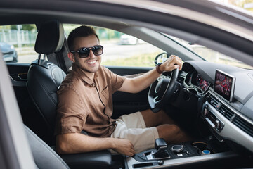 Handsome young man in sunglasses sitting in his luxury car and looking into camera. Smart young man...