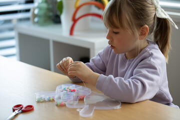 A sweet girl enthusiastically makes a bracelet of beads. A creative child engaged in jewelry making
