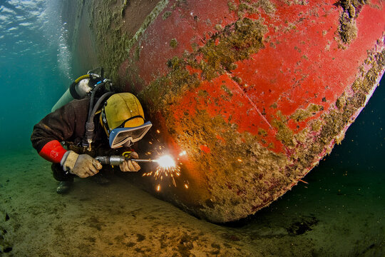 Underwater welder repairing the hull of a ship with sparks flying, in the depths of the ocean