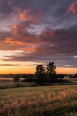 A 4K time-lapse photo of a majestic sunset over a field. The sky is filled with stunning nature's light and rolling colorful clouds. The field is golden and the horizon line is clear. 