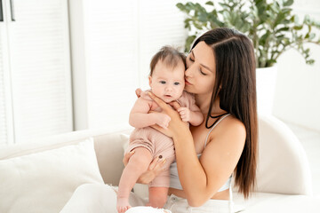 mom with a newborn baby, a young mother holds a small newborn baby in her arms, gently hugging and kissing him at home in a bright room, happy motherhood