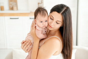 mom with a newborn baby, a young mother holds a small newborn baby in her arms, gently hugging and kissing him at home in a bright room, happy motherhood