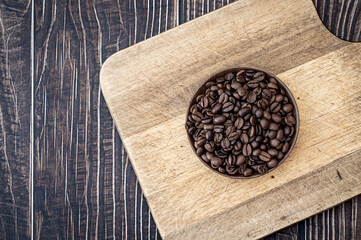 coffee beans in wooden bowl on cutting board with dark wood background