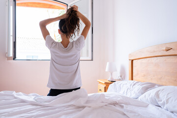 Woman putting up her hair in the morning sitting on her back in bed. Early morning concept