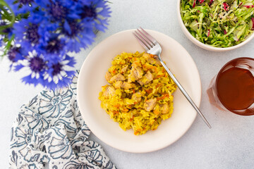 Stewed rice with chicken breast and mixed salad with radishes and various seeds, a served table with food and a vase of flowers, a delicious hearty lunch or dinner