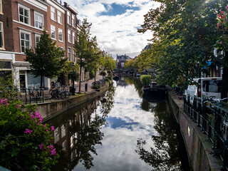 Fototapeta premium Leiden’s canals, lined with historic Dutch buildings and lush greenery, reflect the serene beauty of the city. The calm waters and picturesque architecture create a tranquil urban scene.