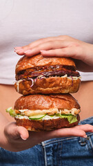 Delicious stacked burgers held by a smiling person against a casual backdrop, showcasing mouthwatering toppings and fresh ingredients at lunchtime