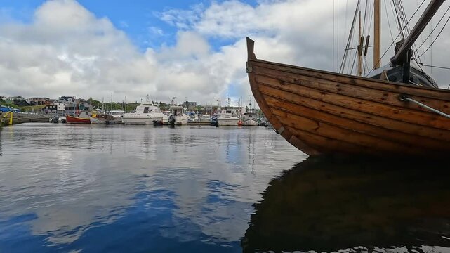 Clouds reflect upon the water in a beautiful Harbor in T&oacute;rshavn, the capital city of the Faroe Islands. Wooden fishing boat on the North Atlantic Ocean.  Remote Nordic city on the island of Streymoy.