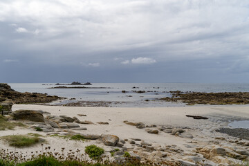 Une plage du Finist&egrave;re nord en Bretagne, &agrave; mar&eacute;e basse, o&ugrave; le sable est parsem&eacute; de rochers et d'&eacute;cueils partiellement immerg&eacute;s, sous un ciel d'&eacute;t&eacute; sombre et mena&ccedil;ant.