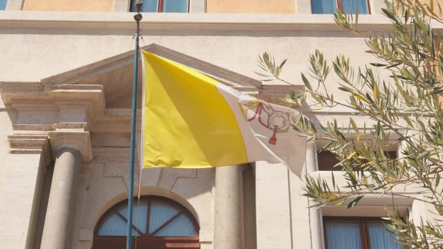 The Vatican flag waves softly amid grand architecture and olive trees