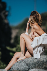 Young woman with a tattoo sitting on a rock in a natural setting, enjoying a sunny day outdoors.