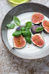 Grey plate with greek yogurt, sliced fig fruits and basil, vertical shot on a light-brown granite surface, middle closeup