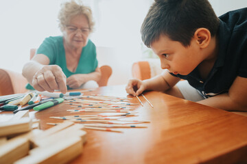 A young boy and his grandmother enjoying a playful moment with a pick-up sticks game in a warm, cozy living room setting.