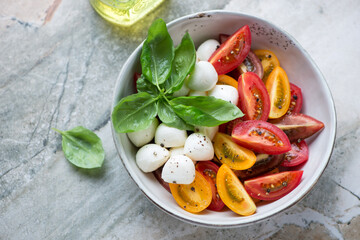 Bowl of caprese with heirloom tomatoes, mini mozzarella and fresh basil, horizontal shot on a grey granite background, elevated view
