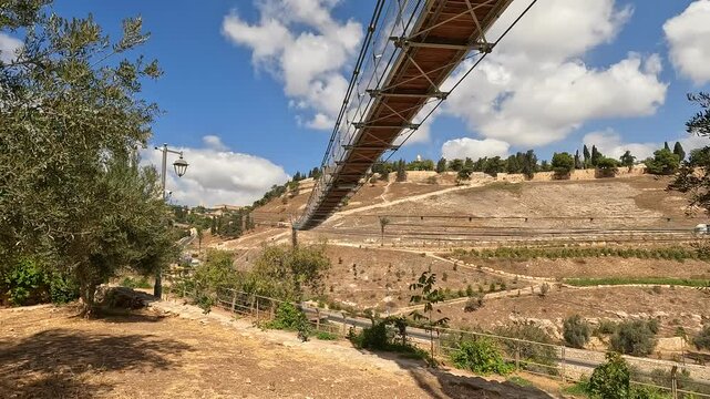the suspension bridge over Gei Ben Hinnom near the Old City of Jerusalem, with the Mount of Olives and cloudy skies in the background. 