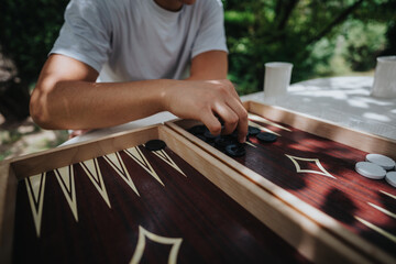 A young person engaged in a game of backgammon outdoors, showcasing strategy and relaxation under the sun.