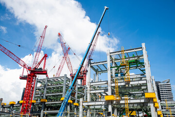Low-angle view of cranes and steel structures of building construction with a blue sky background in Taiwan.