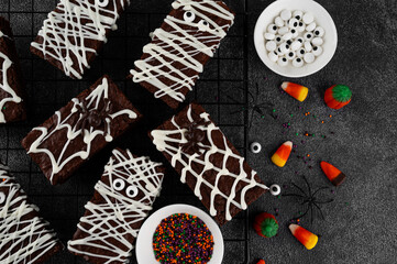 Halloween dessert. Chocolate brownie decorated with chocolate icing in the shape of a mummy and with a spider on a web. Top view, copy space.