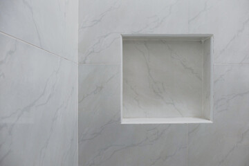 Close up of empty built-in shower caddy in wall recess in bathroom. Modern elegant bathroom interior with marble wall tiles. Display shelf for toiletries logo branding mockup