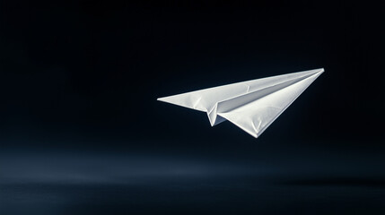 A paper airplane in white, dramatically lit from beneath, set against a dark backdrop to emphasize its clean lines and elegant form. photo