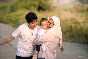 A family that looks happy with lots of laughter with mother, father and baby boy. mother holding a baby boy with a surprised expression while smiling and smiling at the baby boy.