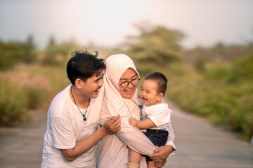 Fototapeta premium A family that looks happy with lots of laughter with mother, father and baby boy. they laughed while teasing the baby boy. father and mother smile seeing the baby boy. photo atmosphere in nature.