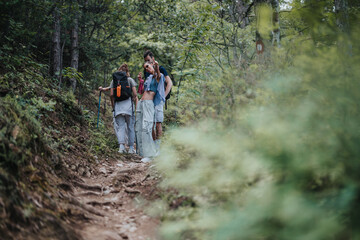 Obraz premium A group of friends enjoying a hike in the forest, with one of them pointing at the camera. The trail is surrounded by lush greenery.