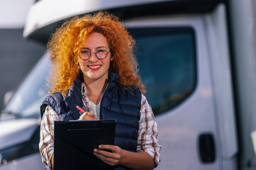 Ginger woman truck driver standing in front of her truck with a paper and write something....