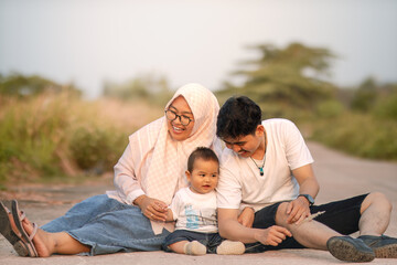 A family that looks happy with lots of laughter with mom, dad and baby boy. everyone laughs happily facing the camera while sitting together. photo atmosphere in peaceful and beautiful nature.