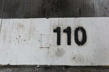 close up of black number one hundred and ten (110) painted on the white floor taken in car park that is old and torn out with copy space