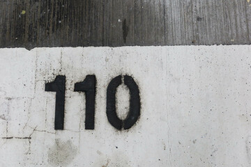 close up of black number one hundred and ten (110) painted on the white floor taken in car park that is old and torn out with copy space