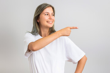 Cheerful young woman pointing finger at blank copy space. Isolated on grey background.