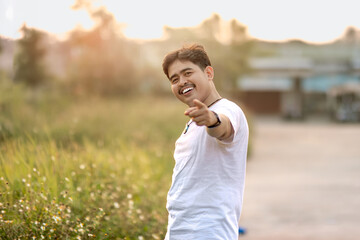 Fototapeta premium a man standing and smiling. the man points at the camera in the sunny afternoon.