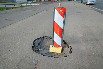 Barrier around sidewalk pit, stripped barrier at sinkhole. Damaged asphalt pavement. Pit on the...