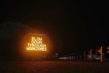 Slow down through work zones, night time illuminated road warning sign. Australia Outback. Rural...